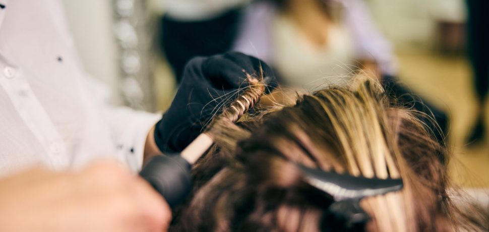 A skilled hairstylist wearing gloves curls a client's hair using a curling iron in a modern salon.